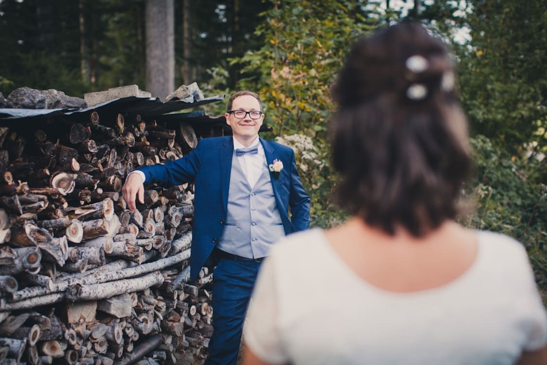 Bräutigam lehnt an einem Holzscheit und sieht zu seiner Braut hinüber