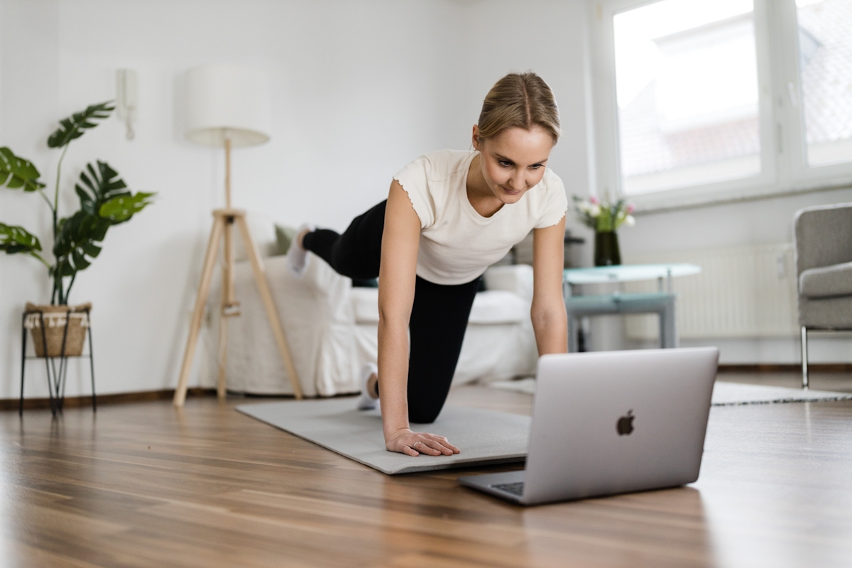 Frau macht Gymnastikübungen zu Hause vor dem Laptop