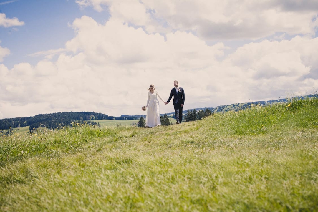 Brautpaar läuft über Wiese mit blauem Himmel und großen weißen Wolken