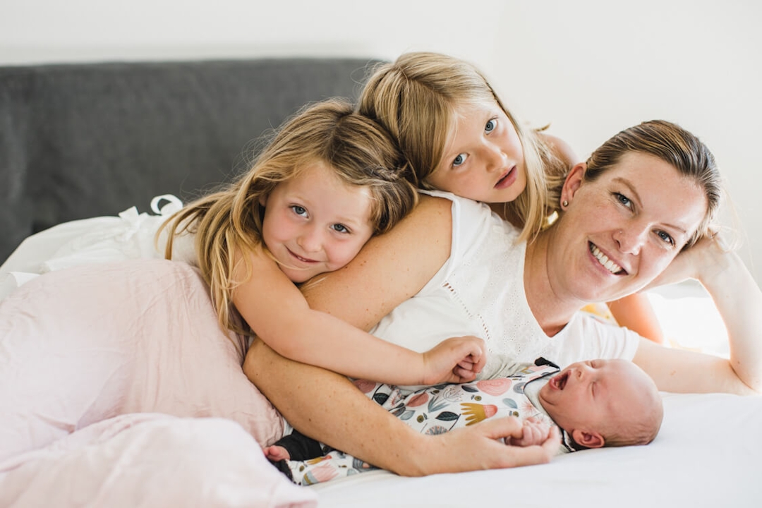 Mutter liegt auf dem Bett mit ihrem Neugeborenen und ihren beiden Töchtern