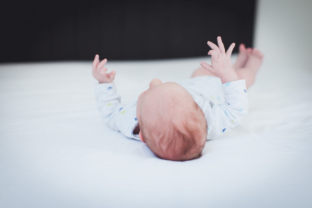 Hinterkopf und Hände von einem Neugeborenen Baby das auf einem Bett liegt