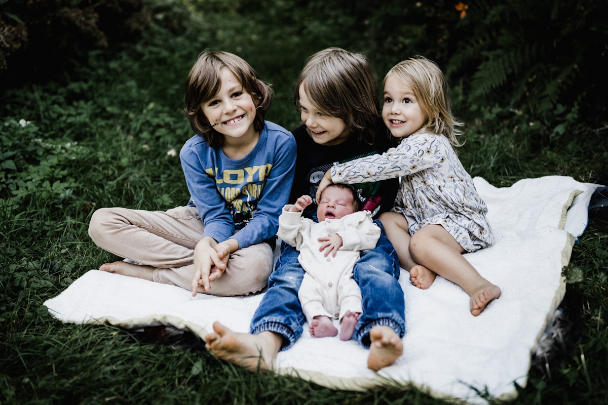 Baby mit Geschwistern auf einer Decke im Garten