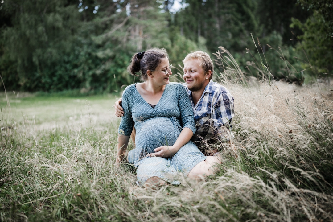 Schwangere Frau mit Mann sitzt auf einer Wiese und schauen sich an