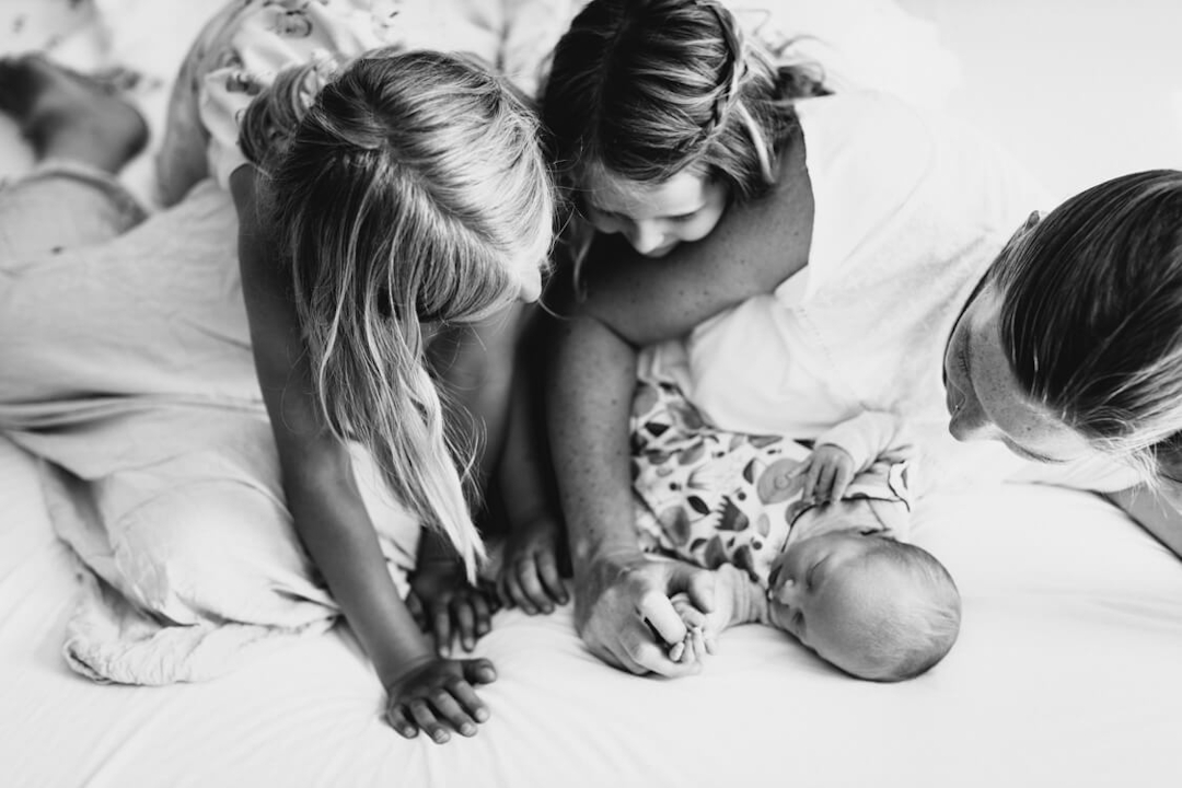 Perspektive von oben wie Mutter und ihren beiden Töchter auf dem Bett liegen und sich zum Neugeborenen beugen