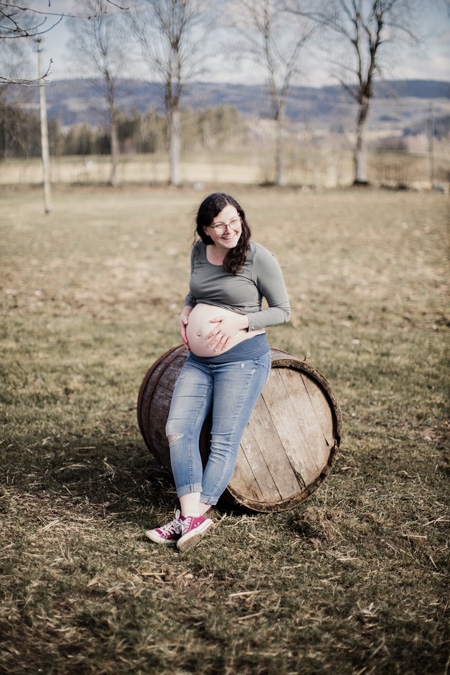 Schwangere Frau sitzt auf einem Weinfass