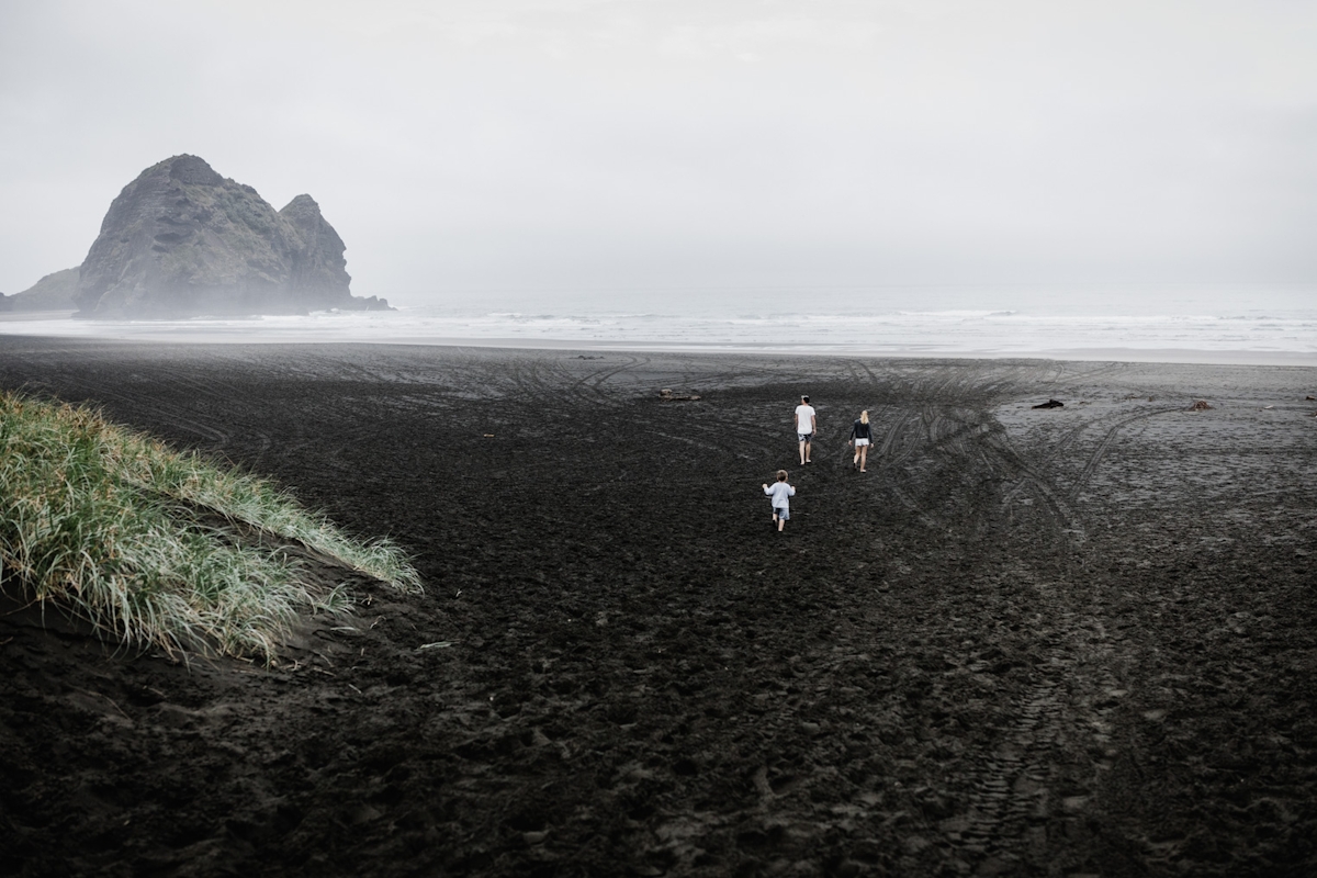 Drei Menschen laufen über schwarzen Sandstrand 