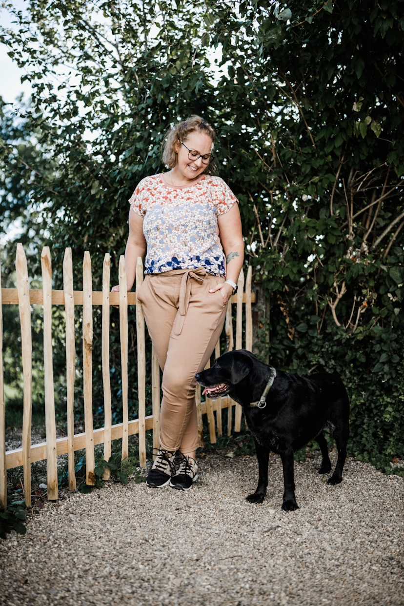Frau mit Hund am Gartenzaun stehend