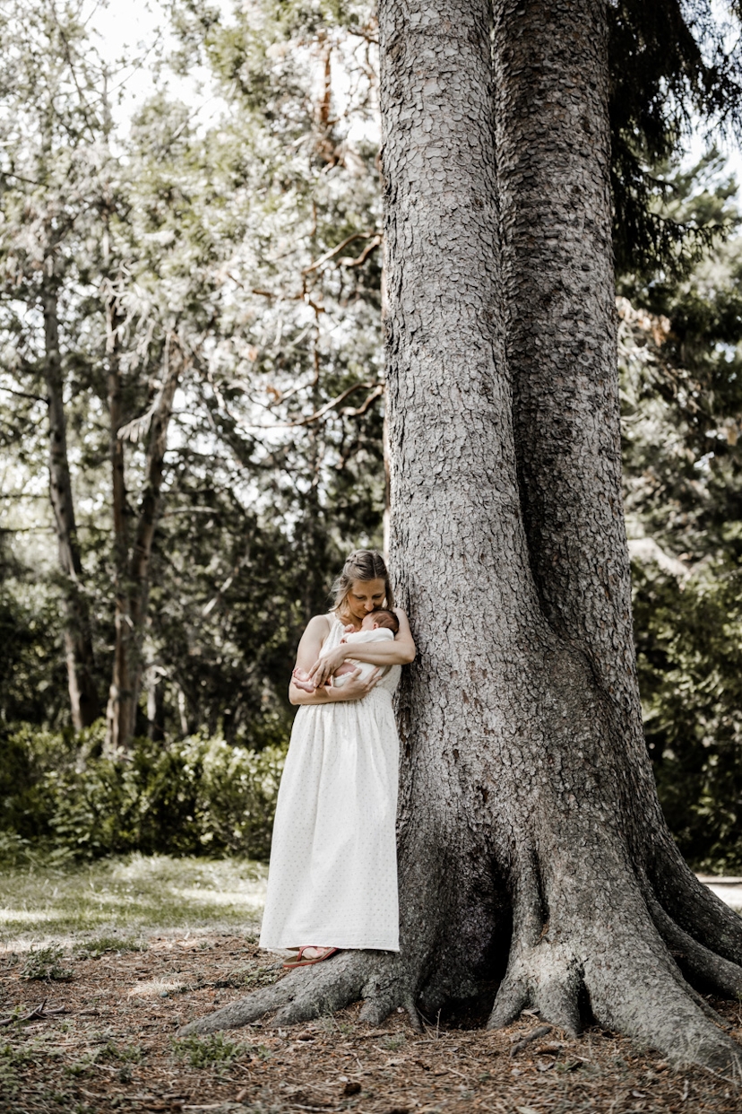 Frau mit Baby auf dem Arm lehnt an einem Baum